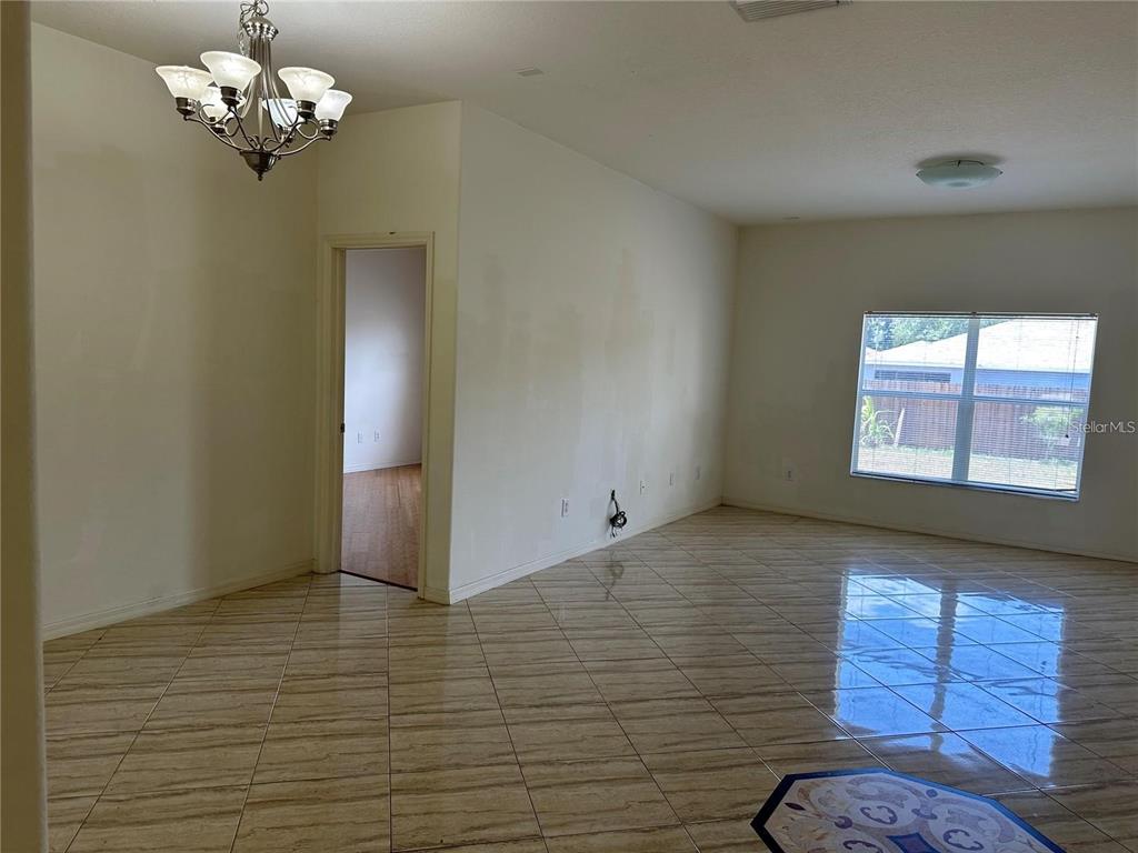 An empty room features light-colored tile flooring, a chandelier, and a doorway leading to another room — 903 COADE STONE DRIVE, SEFFNER, FL