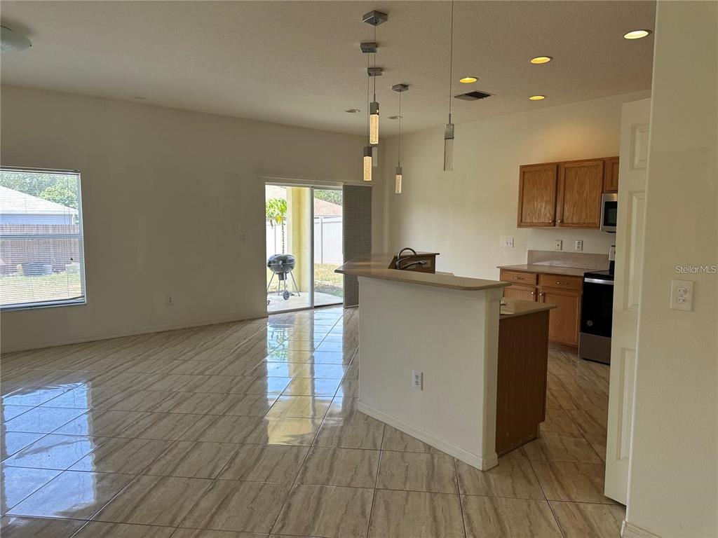 An open-concept kitchen and living area features tile flooring, pendant lighting, and a sliding door — 903 COADE STONE DRIVE, SEFFNER, FL