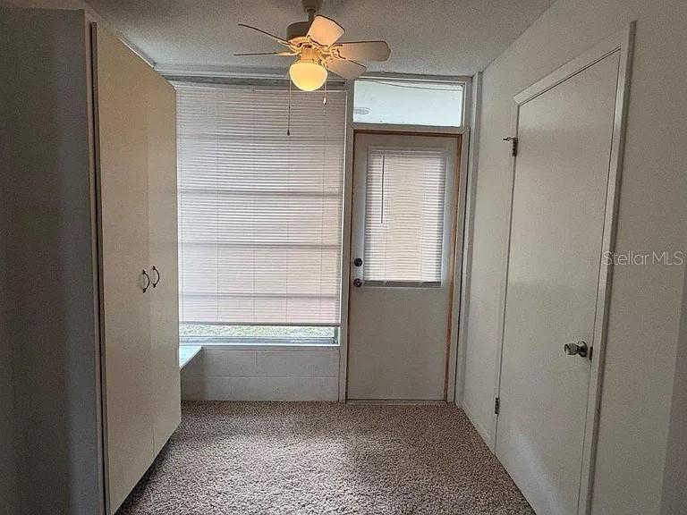 A small room with carpeted flooring, a ceiling fan, a large window, and two doors — 720B E MINNESOTA AVENUE UNIT B, DELAND, FL