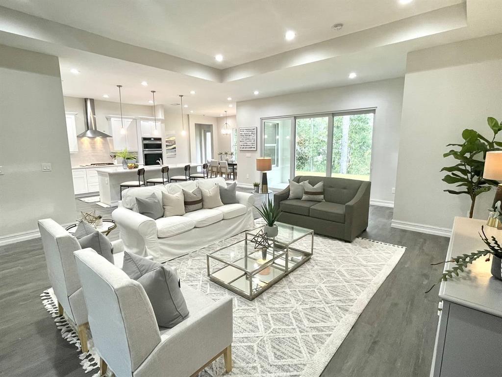 An open-concept living room features a white sofa, gray loveseat, and a modern kitchen — 1973 NW 85TH LOOP, OCALA, FL