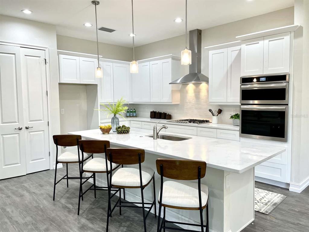 A modern kitchen features white cabinetry, a marble-topped island with four stools, and stainless appliances — 1973 NW 85TH LOOP, OCALA, FL