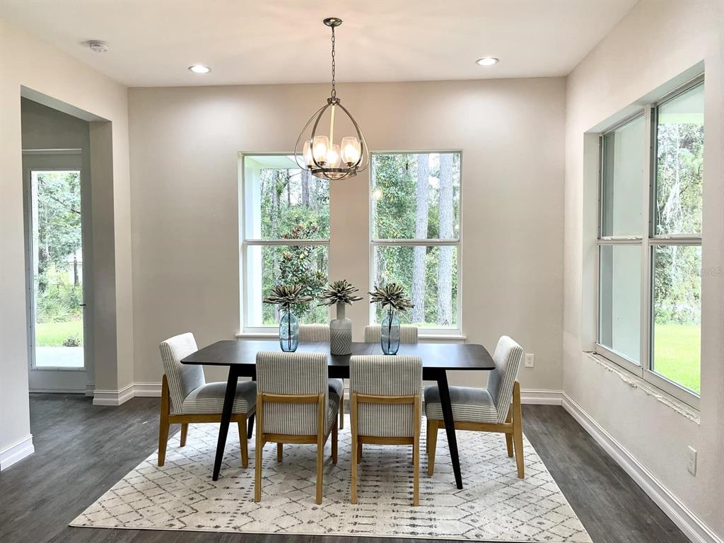 A dining room features a dark table, six striped chairs, a chandelier, and large windows — 1973 NW 85TH LOOP, OCALA, FL