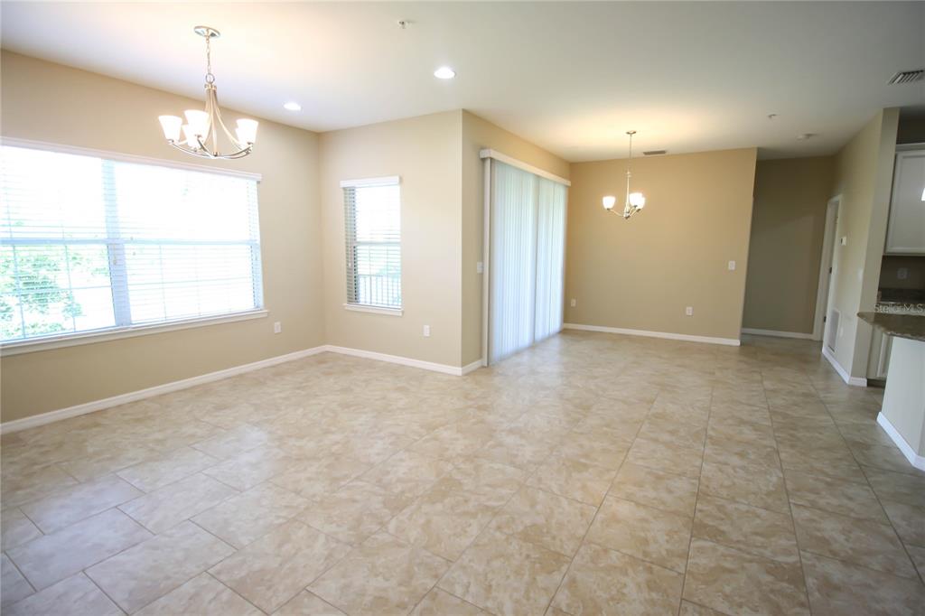 An open-concept dining area features beige walls, tile flooring, two chandeliers, and sliding glass doors — 4248 EXPEDITION WAY, OSPREY, FL