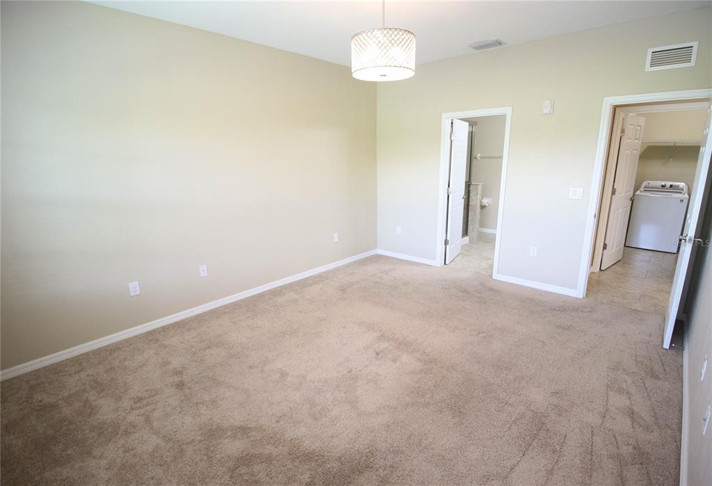 A carpeted bedroom features beige walls, a central light fixture, and two open doorways — 4248 EXPEDITION WAY, OSPREY, FL