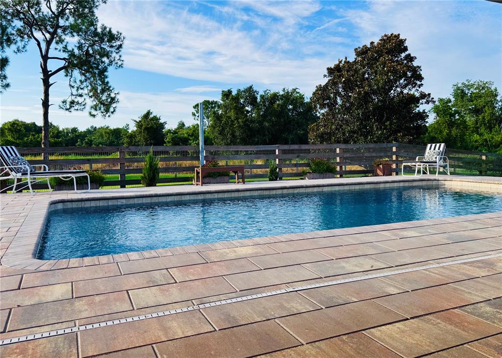 A rectangular swimming pool sits on a paved patio with lounge chairs and a wooden fence — 374 CATFISH CREEK ROAD, LAKE PLACID, FL