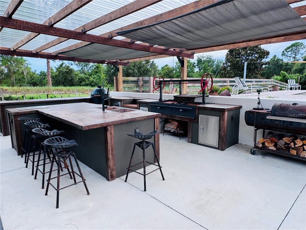 An outdoor kitchen features a wooden island, bar stools, a grill, and a covered patio — 374 CATFISH CREEK ROAD, LAKE PLACID, FL