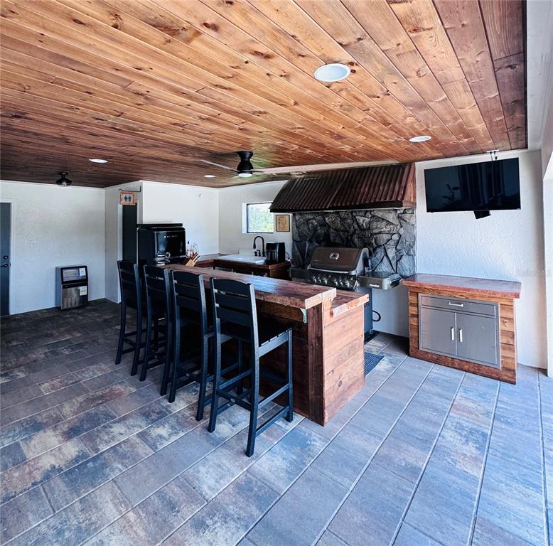 An outdoor kitchen features a wooden bar, stone backsplash, and a wood-paneled ceiling — 374 CATFISH CREEK ROAD, LAKE PLACID, FL