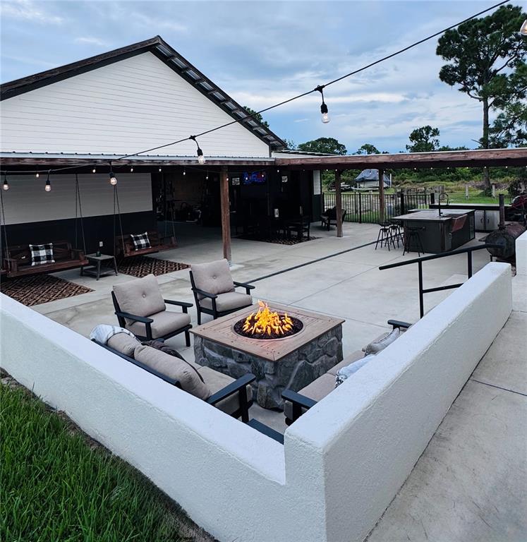 A backyard patio features a stone fire pit, lounge seating, and a covered outdoor kitchen area — 374 CATFISH CREEK ROAD, LAKE PLACID, FL