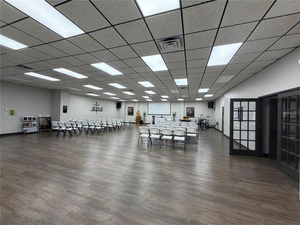 A large, open room with wood-look flooring, a drop ceiling, and rows of white folding chairs — 208 E LAKE AVENUE, AUBURNDALE, FL