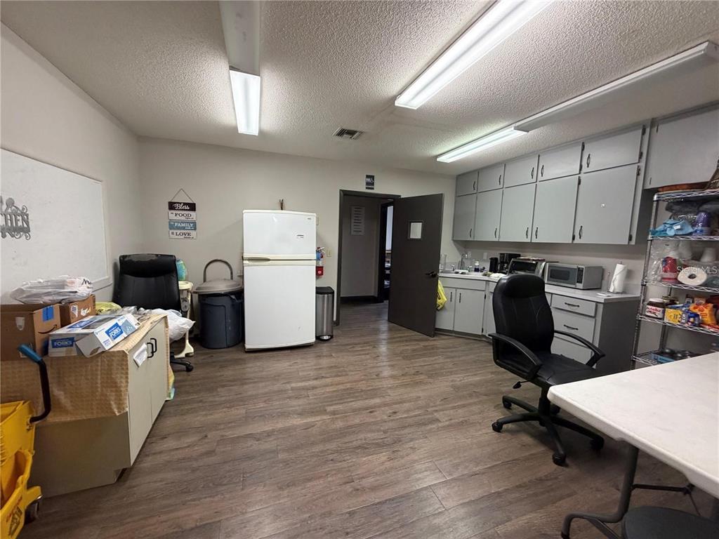 A breakroom features gray cabinetry, a white refrigerator, wood-look flooring, and two office chairs — 208 E LAKE AVENUE, AUBURNDALE, FL