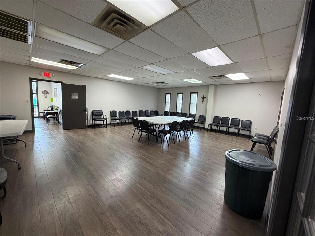 A large, open multipurpose room features wood-look flooring, a drop ceiling, and rows of chairs — 208 E LAKE AVENUE, AUBURNDALE, FL