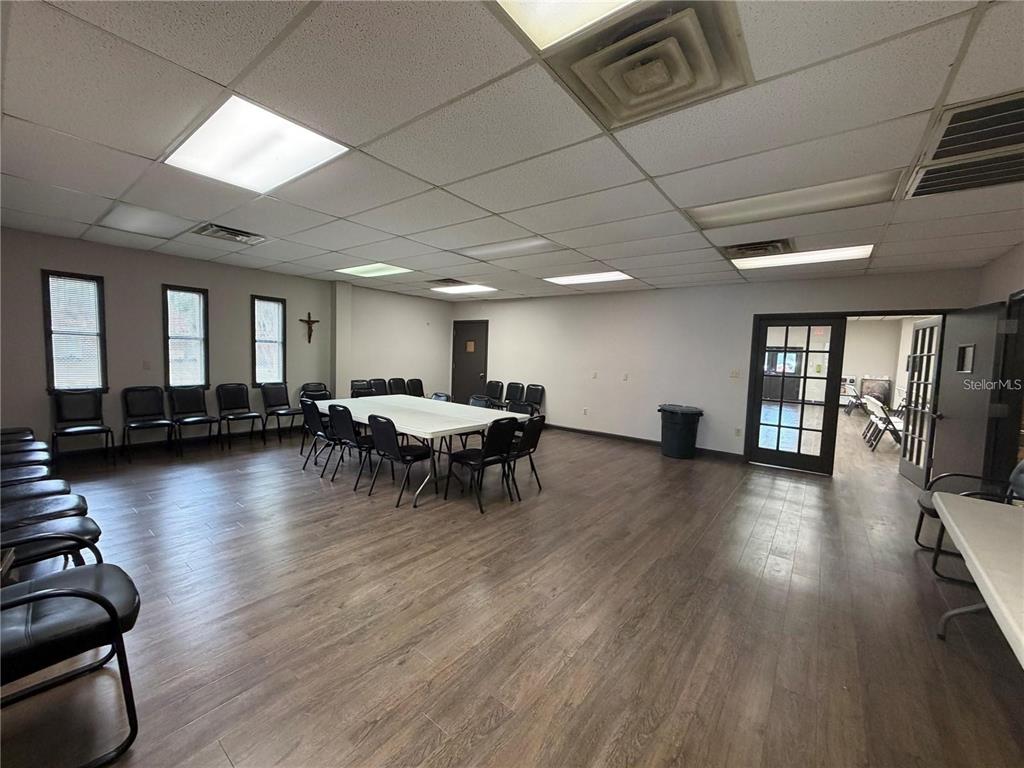 A large multipurpose room features wood-look flooring, a drop ceiling, and rows of black chairs — 208 E LAKE AVENUE, AUBURNDALE, FL