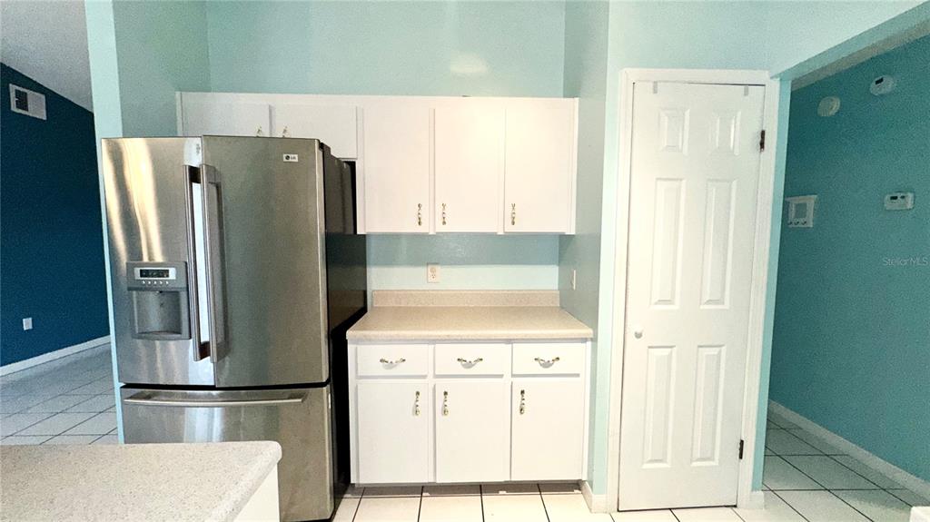 A kitchen features white cabinets, a stainless steel refrigerator, and light-colored countertops — 620 BROCKTON DRIVE, KISSIMMEE, FL