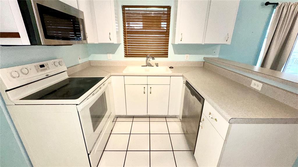 A kitchen features white cabinets, a white stove, a stainless steel dishwasher, and tiled floors — 620 BROCKTON DRIVE, KISSIMMEE, FL