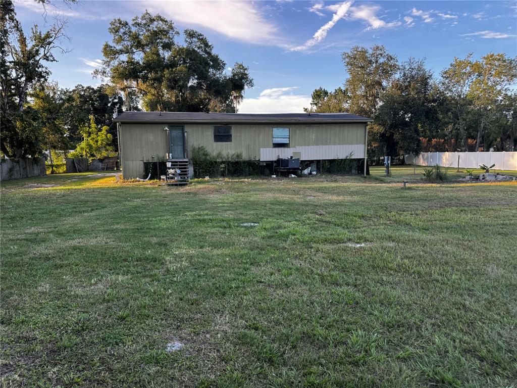 A single-story mobile home with olive green siding sits on a large, grassy lot — 33346 ARTHUR DRIVE, WESLEY CHAPEL, FL