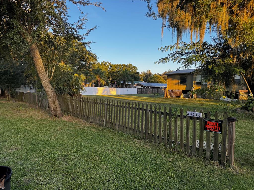 A wooden picket fence encloses a grassy yard with a house in the background — 33346 ARTHUR DRIVE, WESLEY CHAPEL, FL
