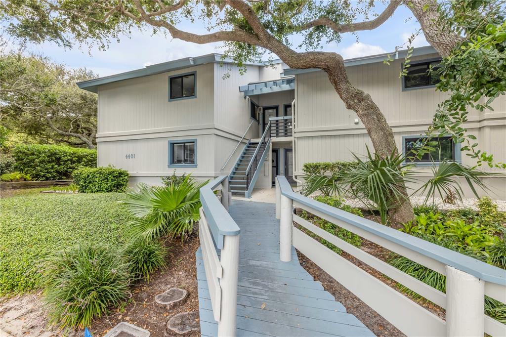 A two-story building exterior features a wooden ramp leading to an outdoor staircase — 4401 SEA MIST DRIVE UNIT 102, NEW SMYRNA BEACH, FL