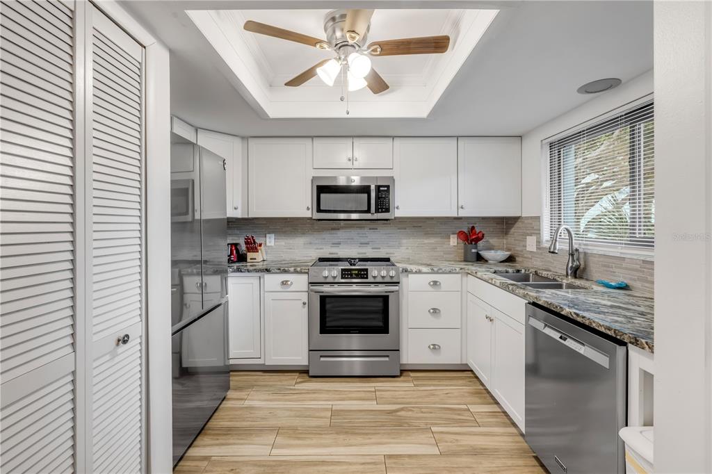 A kitchen features white cabinets, stainless steel appliances, granite countertops, and wood-look tile flooring — 4401 SEA MIST DRIVE UNIT 102, NEW SMYRNA BEACH, FL