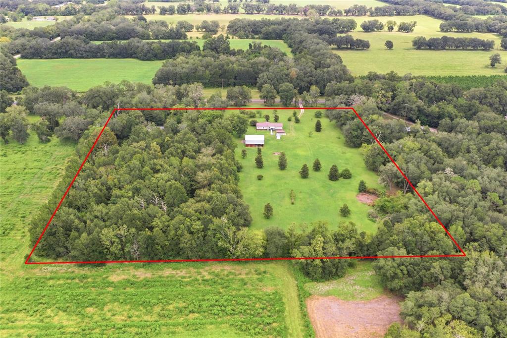 An aerial view shows a rural property with a house, barn, and wooded acreage — 7412 NW STATE ROAD 45, HIGH SPRINGS, FL