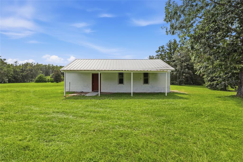 A white, single-story concrete block building with a metal roof sits in a grassy field — 7412 NW STATE ROAD 45, HIGH SPRINGS, FL