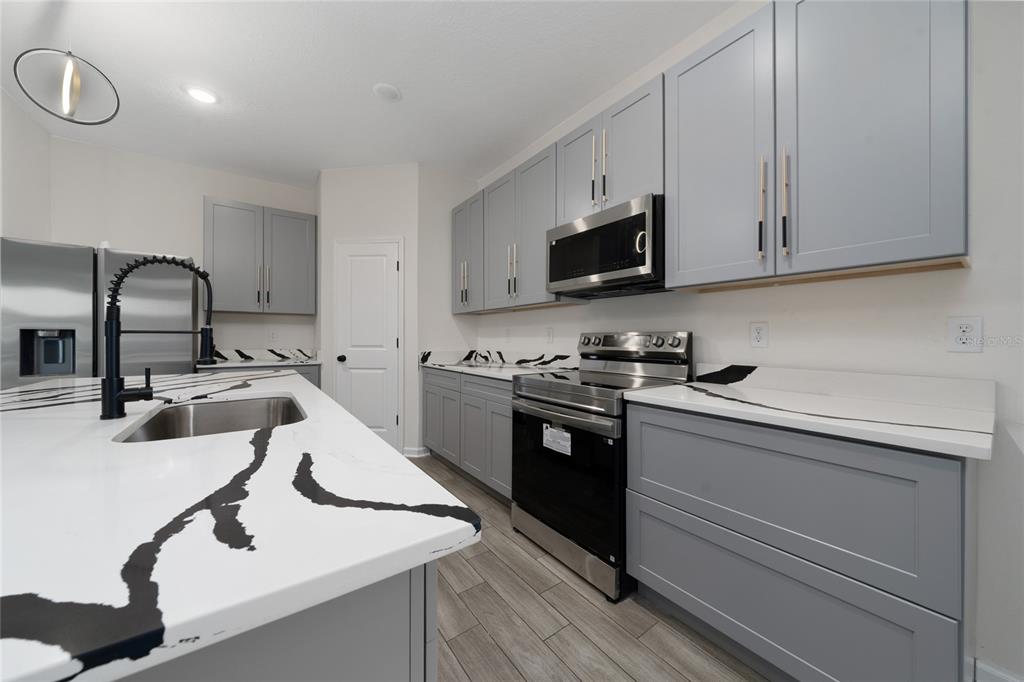 A modern kitchen features gray cabinets, white marble-patterned countertops, and stainless steel appliances — 6404 SPRUCEPINE LANE, ST CLOUD, FL