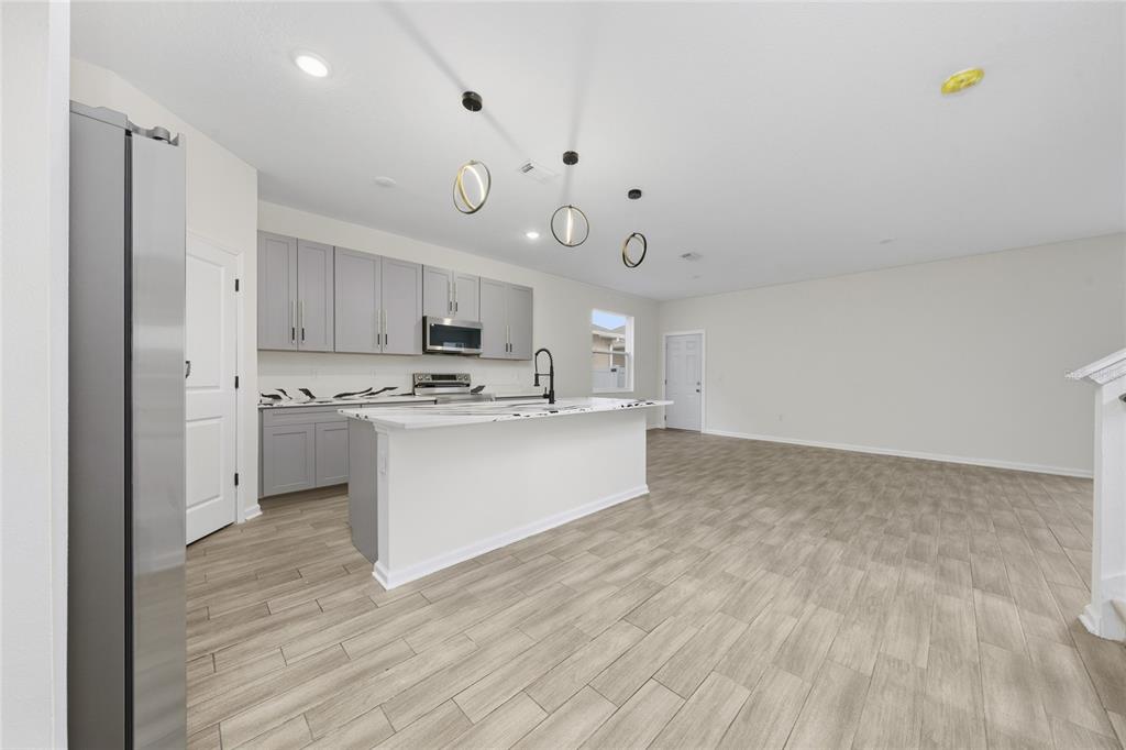 A modern kitchen features gray cabinets, white countertops, and wood-look tile flooring — 6404 SPRUCEPINE LANE, ST CLOUD, FL