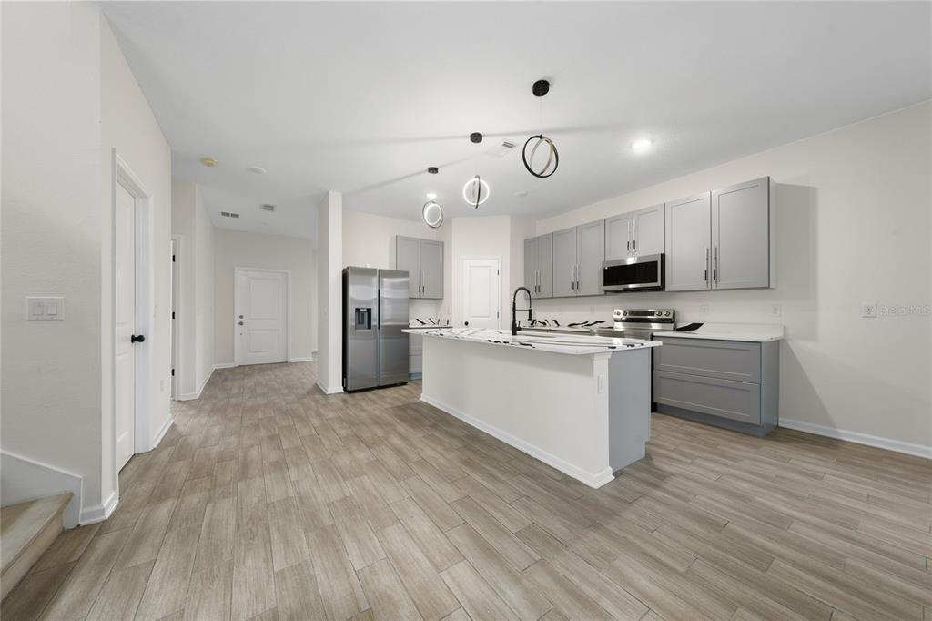 A modern kitchen features gray cabinets, a white marble-topped island, and light wood-look flooring — 6404 SPRUCEPINE LANE, ST CLOUD, FL