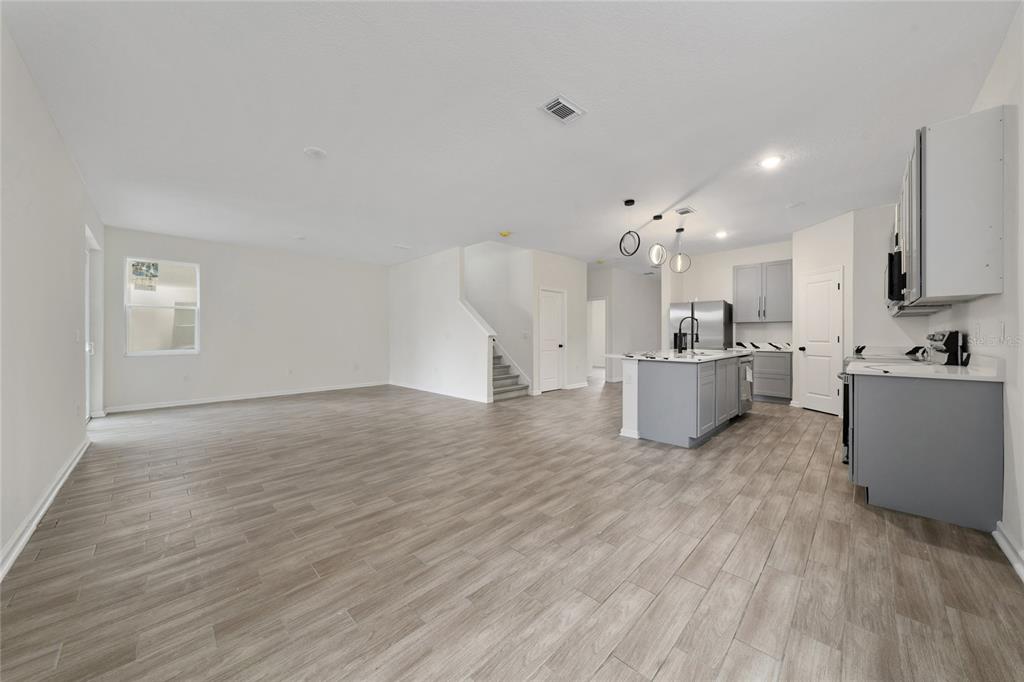 An open-concept living area features light wood-look tile flooring and a kitchen with gray cabinetry — 6404 SPRUCEPINE LANE, ST CLOUD, FL