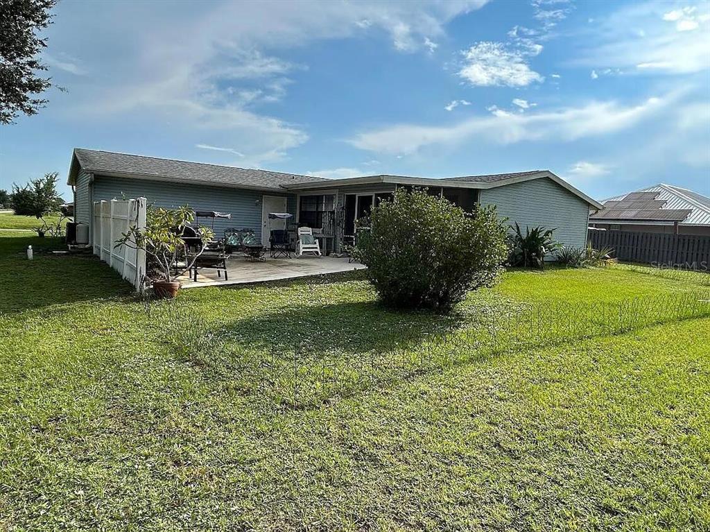 The backyard of a single-story house features a concrete patio and a large green bush — 7901 CASTILE ROAD, SEBRING, FL