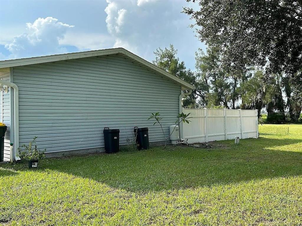 The exterior side of a house with light blue siding, two trash cans, and fencing — 7901 CASTILE ROAD, SEBRING, FL