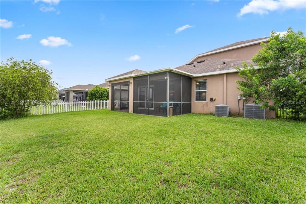A backyard features a grassy lawn, a screened-in patio, and a white picket fence — 8005 112TH AVENUE E, PARRISH, FL