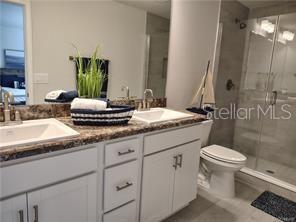 A bathroom features a double vanity with a granite countertop, white cabinets, and a shower — 239 BITTERN LOOP, INVERNESS, FL