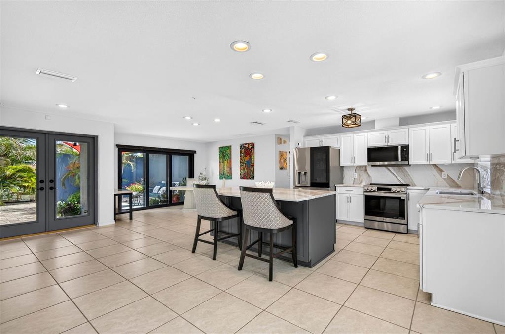 A bright kitchen features a dark gray island, white cabinetry, and tile flooring throughout — 114 12TH STREET, BELLEAIR BEACH, FL