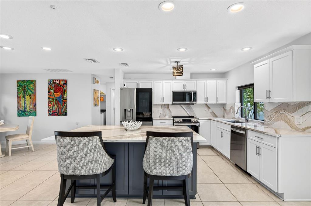 A kitchen with white cabinets, a dark blue island, and marble-patterned countertops and backsplash — 114 12TH STREET, BELLEAIR BEACH, FL
