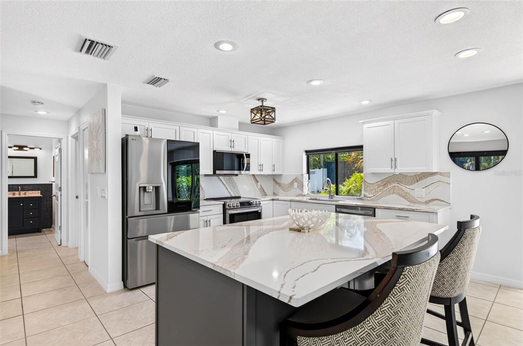 A kitchen features white cabinets, a dark gray island, and a patterned stone backsplash — 114 12TH STREET, BELLEAIR BEACH, FL