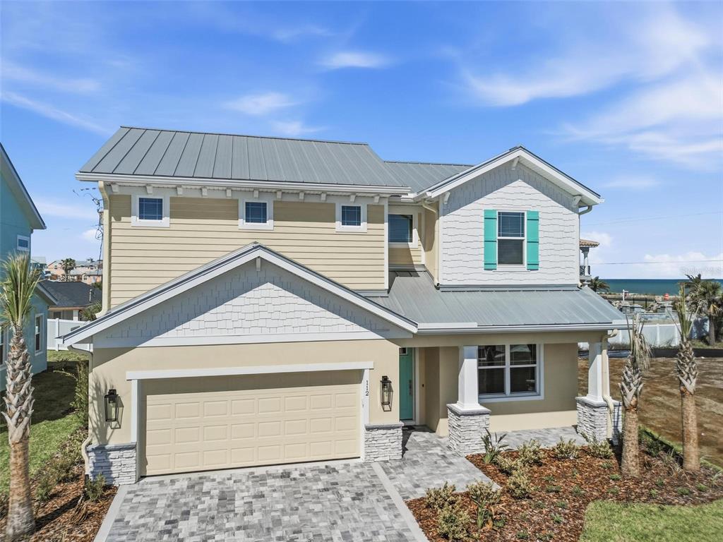 A two-story coastal house features a metal roof, tan siding, and a paved driveway — 112 BEACHVIEW DRIVE, ORMOND BEACH, FL