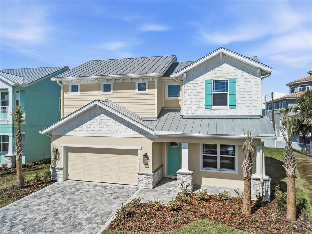 A two-story house with a metal roof, tan siding, and a paved driveway — 112 BEACHVIEW DRIVE, ORMOND BEACH, FL