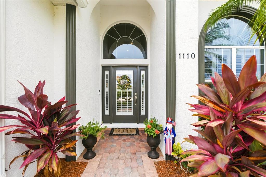 A paved walkway leads to a front entrance with a decorative door and arched window — 1110 3RD STREET E, PALMETTO, FL