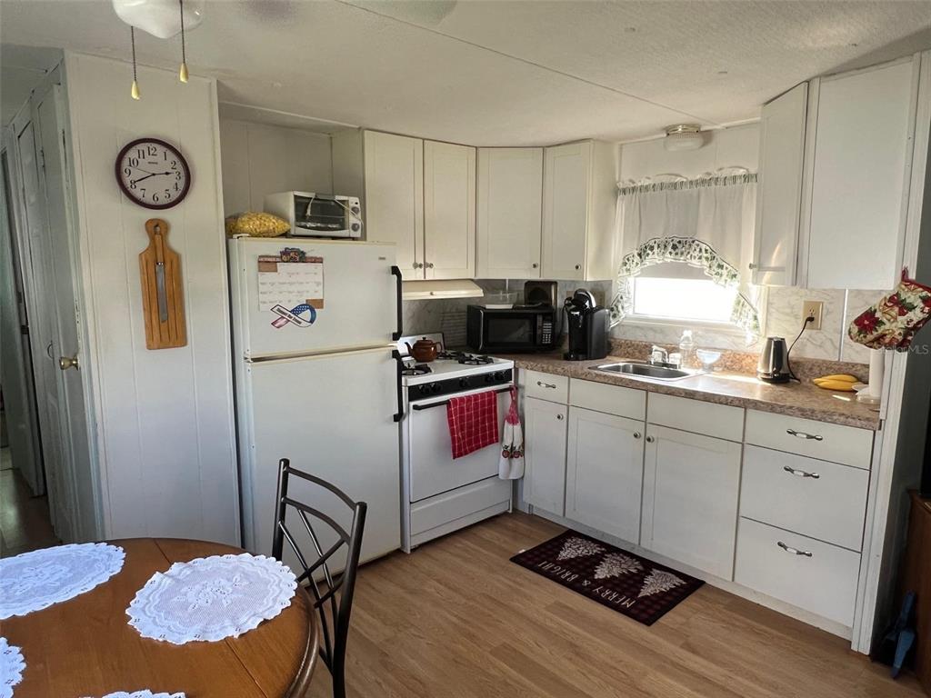 A kitchen features white cabinets, white appliances, a wooden table, and a window with curtains — 12674 SEMINOLE BOULEVARD UNIT C6, LARGO, FL