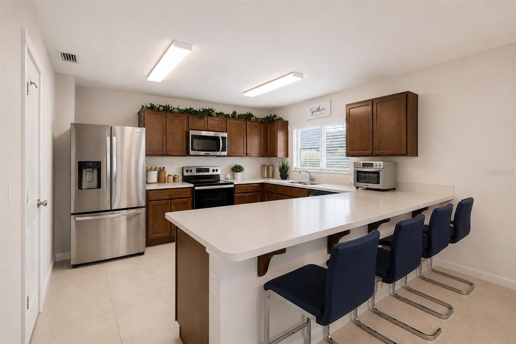 A kitchen features dark wood cabinets, stainless steel appliances, a white countertop, and bar seating — 3110 SANCTUARY DRIVE, CLERMONT, FL