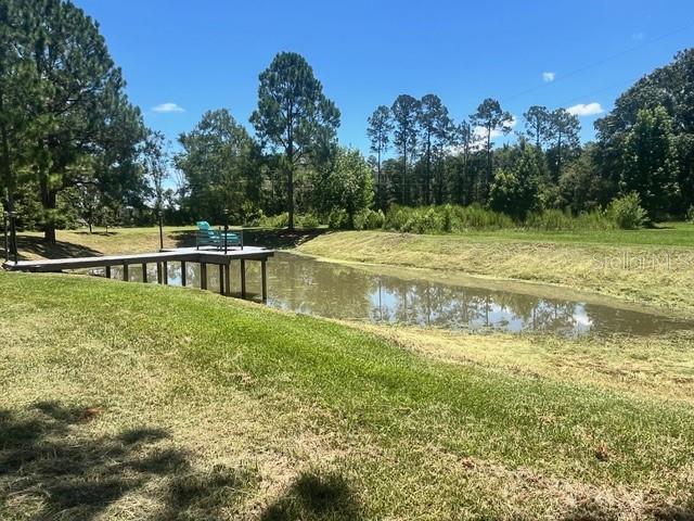 A wooden dock with a chair extends over a small pond surrounded by grassy land — 9559 SE STATE ROAD 100, STARKE, FL