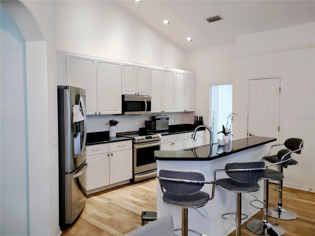 A kitchen features white cabinets, black countertops, stainless steel appliances, and a breakfast bar — 11939 56TH STREET E, PARRISH, FL