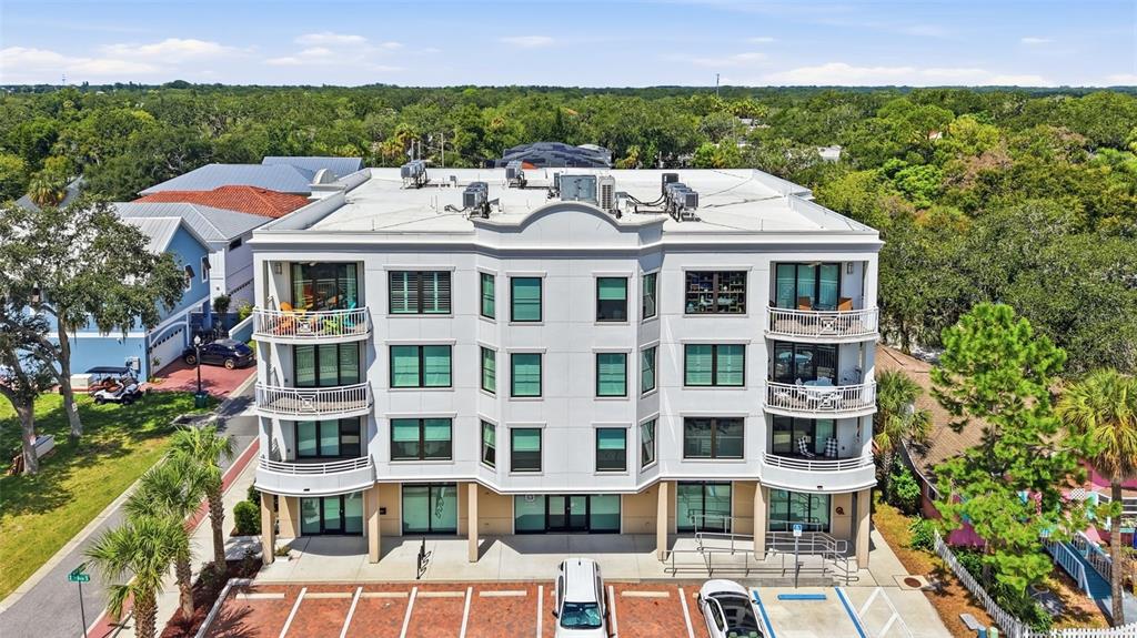 An aerial view of a three-story white apartment building with balconies and a parking lot — 231 2ND STREET S UNIT 202, SAFETY HARBOR, FL