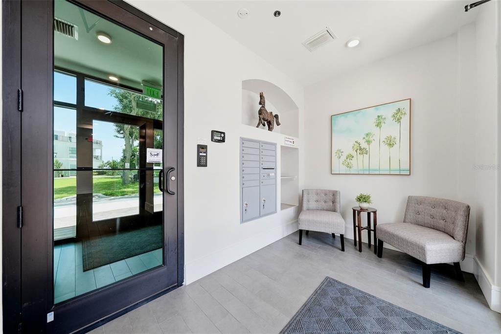 A modern building lobby features a glass door, gray tile floors, mailboxes, and two chairs — 231 2ND STREET S UNIT 202, SAFETY HARBOR, FL