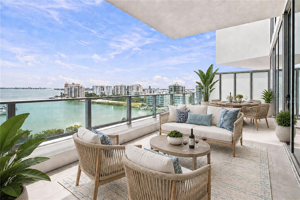 A furnished balcony overlooks a bay with a view of distant buildings under a blue sky — 1155 N GULFSTREAM AVENUE UNIT 806, SARASOTA, FL