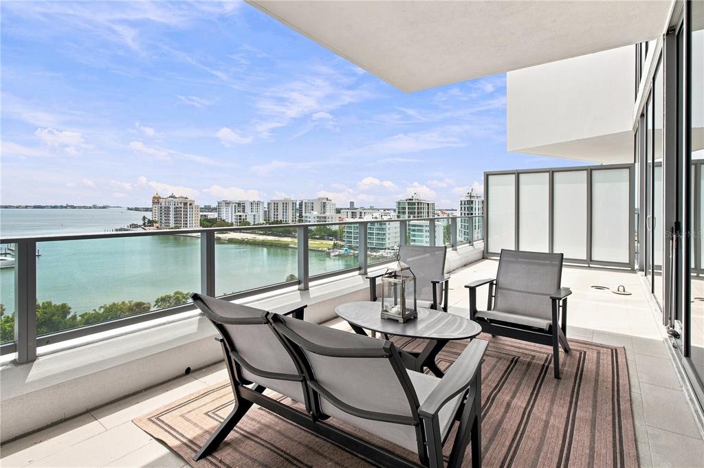 A balcony with outdoor furniture overlooks a bay and city skyline under a blue sky — 1155 N GULFSTREAM AVENUE UNIT 806, SARASOTA, FL
