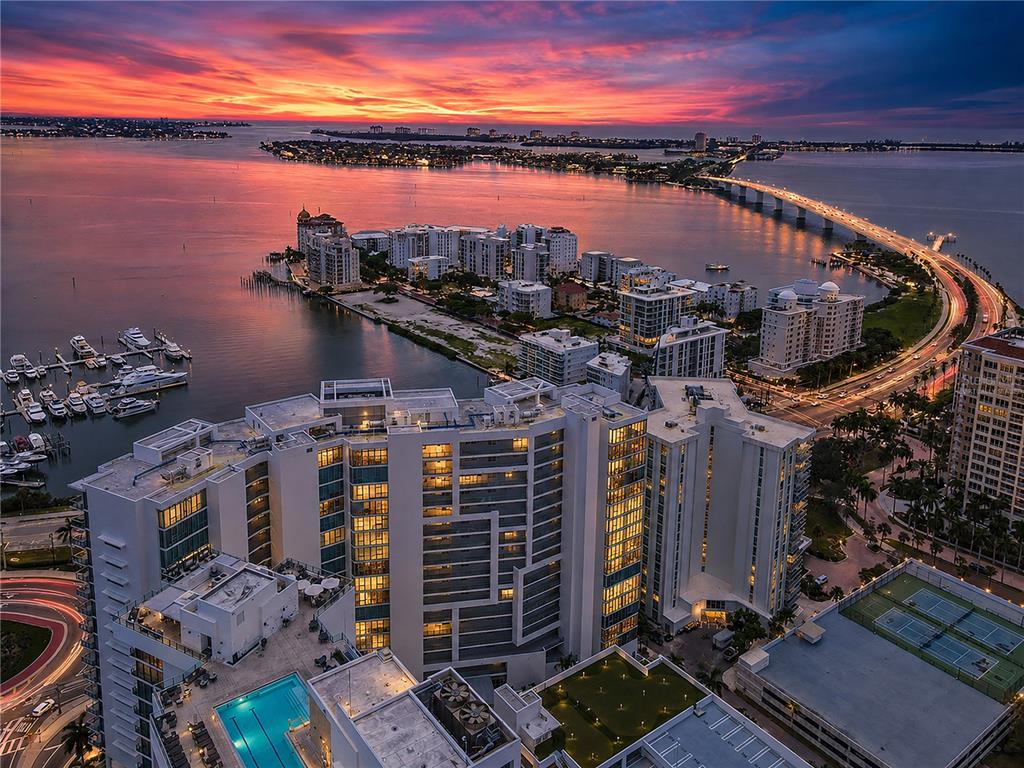 An aerial view of a high-rise condominium complex at sunset near a bridge and water — 1155 N GULFSTREAM AVENUE UNIT 806, SARASOTA, FL