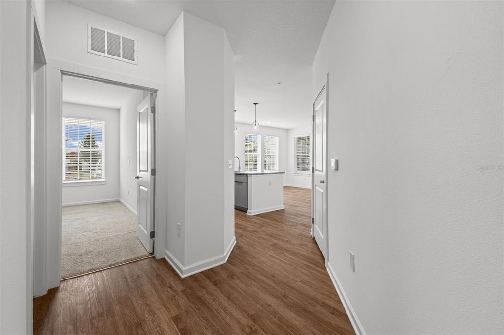 A hallway with wood-look flooring leads to a kitchen and a carpeted room — 1700 RANCH ROAD UNIT B2-6406, NOKOMIS, FL
