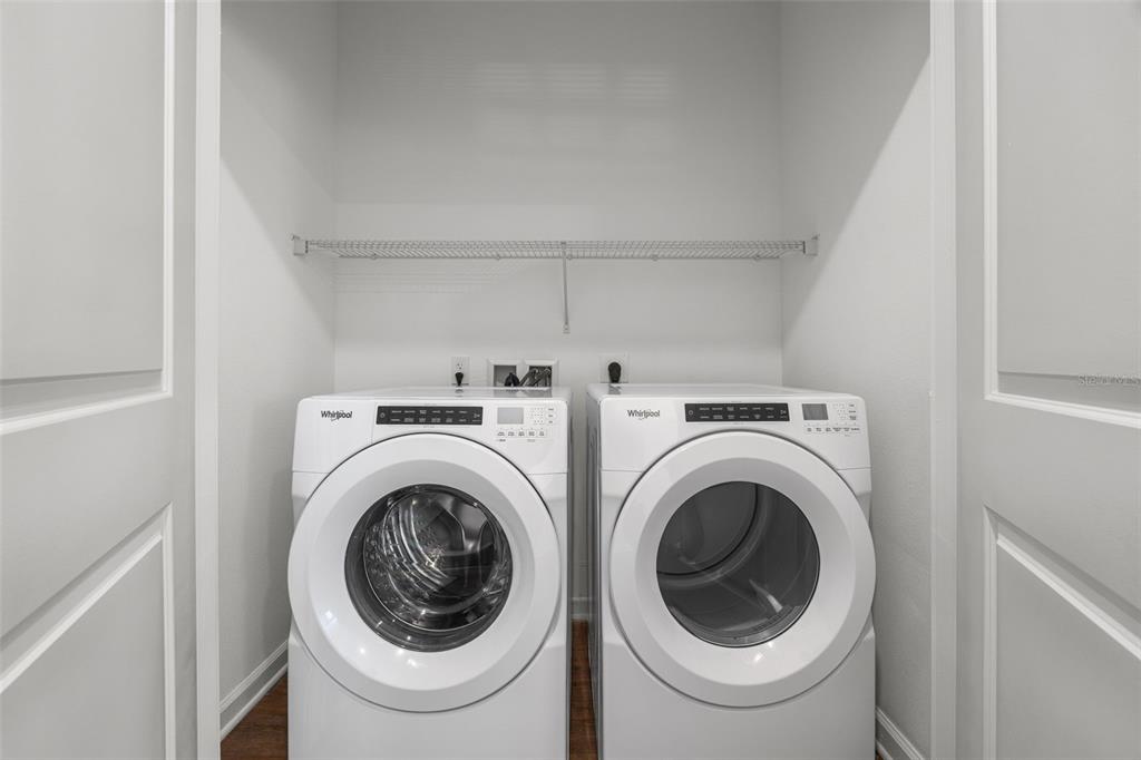 A laundry closet contains a white Whirlpool washer and dryer beneath a wire shelf — 1700 RANCH ROAD UNIT B2-6406, NOKOMIS, FL