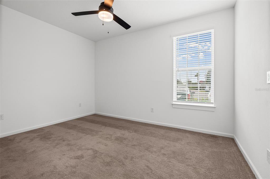 An empty bedroom features white walls, tan carpeting, a ceiling fan, and a single window — 1700 RANCH ROAD UNIT B2-6406, NOKOMIS, FL
